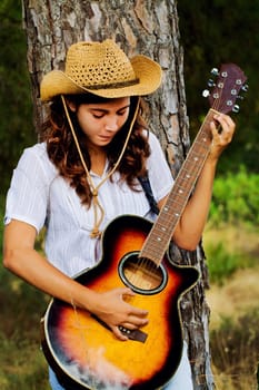 View of a beautiful young country girl with a guitar on the woods. 