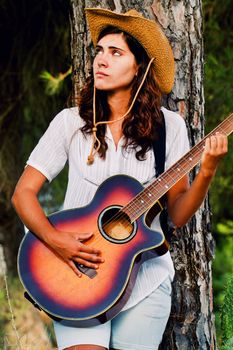 View of a beautiful young country girl with a guitar on the woods. 