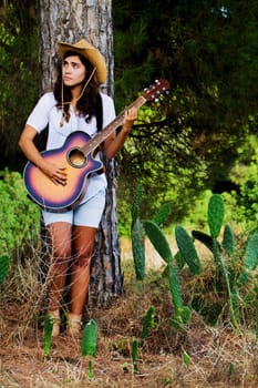 View of a beautiful young country girl with a guitar on the woods. 