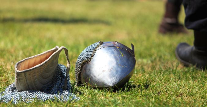 Image of a steel helmet and a chainmail hood on a filed after a medieval fight in a sunny day.