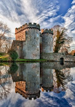 Ancient Whittington Castle in Shropshire, England reflecting in a calm moat round the stone buildings and processed in HDR