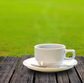 Hot coffee on wooden table with green grass background