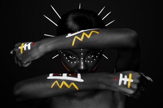 Beautiful cultural tribal African female face with arms and hands in fron, yellow, red and white makeup cosmetics lines dots, sticks in hair.