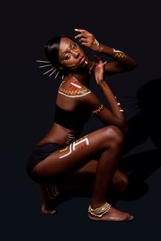 Beautiful exotic African female fashion with tribal yellow red and white makeup cosmetics and sticks in hair, in cultural dance position.