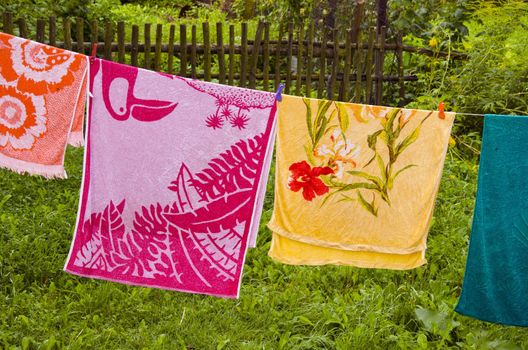 Multicolor towels hanging on string in farmstead. Wooden fence in background.