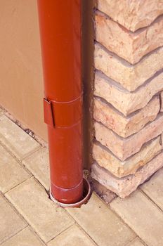 Red rainwater pipe made of tin on house corner made of decorative bricks.