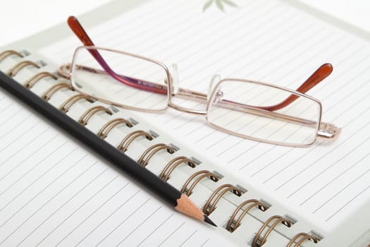 A ruled diary, reading glasses and black pencil