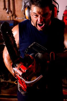 View of a angry garage mechanic man holding a chainsaw.