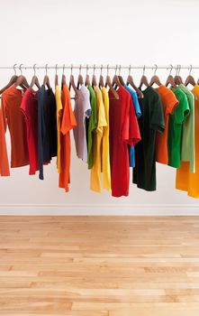 Variety of multicolored casual clothes on a rod, in a bright room.