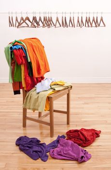 Colorful messy clothes on a chair and row of empty hangers on the background.