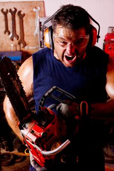 View of a angry garage mechanic man holding a chainsaw.