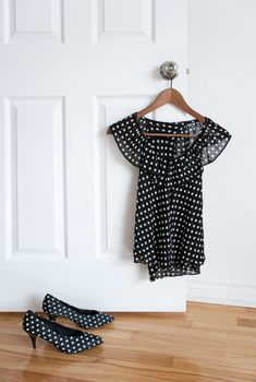 Black and white polka dot shoes and stylish blouse on a hanger.