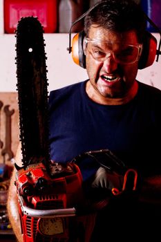 View of a angry garage mechanic man holding a chainsaw.