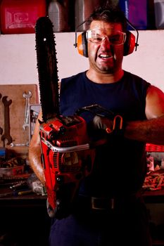 View of a angry garage mechanic man holding a chainsaw.