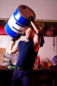 View of a happy garage mechanic man holding an oil barrel.