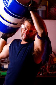 View of a happy garage mechanic man holding an oil barrel.