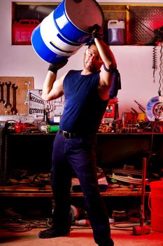 View of a happy garage mechanic man holding an oil barrel.