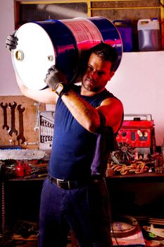 View of a happy garage mechanic man holding an oil barrel.