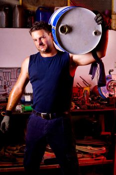 View of a happy garage mechanic man holding an oil barrel.