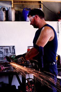 View of a garage mechanic man cutting iron with a power saw creating sparks.