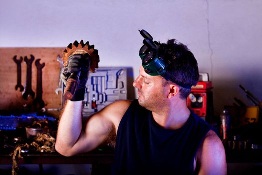 View of a garage mechanic man holding a gear creating muscle.