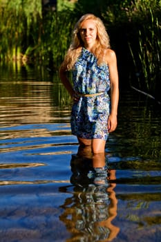 View of a beautiful young girl with a blue dress on the stream of a river.