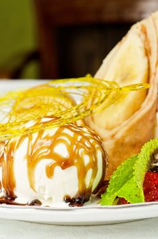 Dessert of pancake with banana, ice-cream, caramel, strawberry and mint