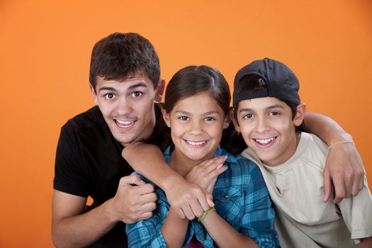 Big brother with two siblings smiling on orange background