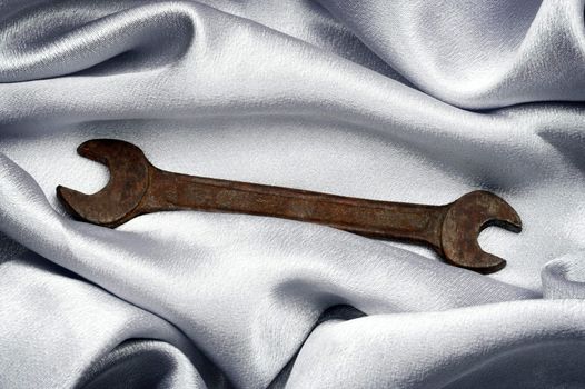 old, rusty wrench over silk background