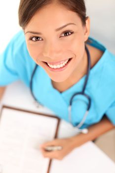 Nurse or woman doctor. Young female medical professional close up portrait. Multi-racial Asian Caucasian model wearing blue srubs and stethoscope from high angle view.