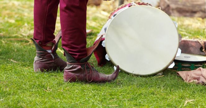Close-up of specific medieval shoes (long toed shoes) on grass near a traditional drum during a medieval festival. The shoes have leather soles and multilayered leather heel made of specially hardened leather.They were popular in 12th-13th centuries in Europe.
