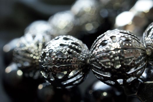 Close up of a bracelet with dark silver beads over black background. Bokeh, soft focus. 