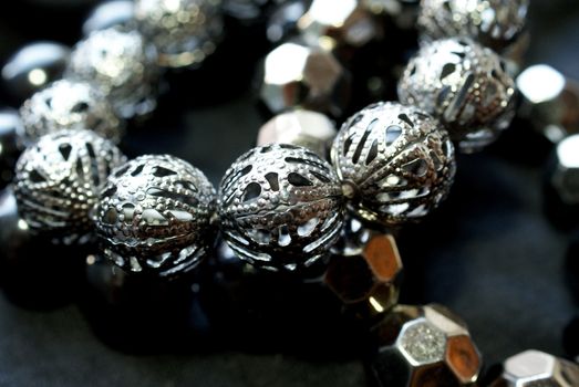 A close up of a bracelet with shiny dark silver beads over black. Soft focus, bokeh effect. 