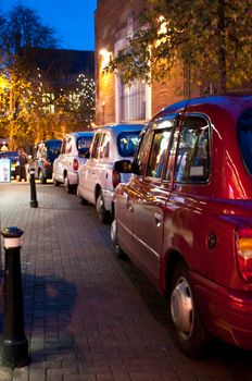 Low level evening shot capturing waiting British taxis in city setting.