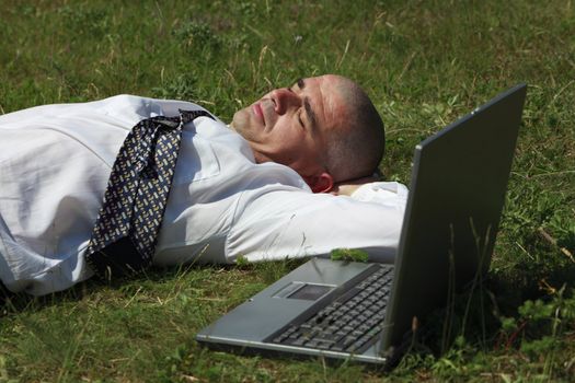 Tired man sleeping in a field near his laptop.