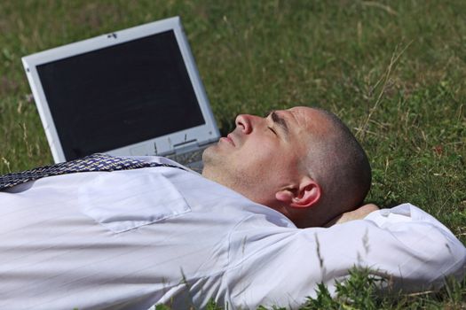 Tired man sleeping in a field near his laptop.