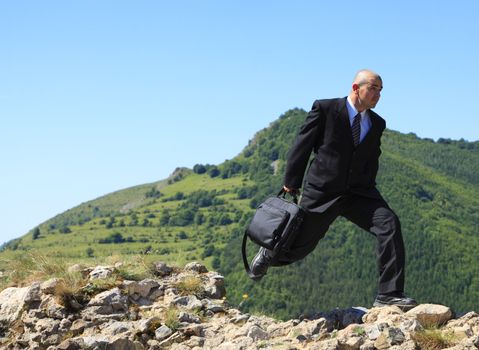 Businessman with a laptop bag running outdoors on a rocky ruined stronghold wall in a mountaineous area.The image can suggest the idea of a thief stealing important data or a man protecting data in case of a disaster.