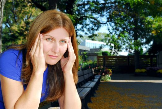 Mature woman with a headache sitting on the park bench