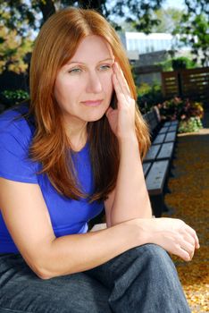 Mature woman looking sad and stressed sitting on a park bench