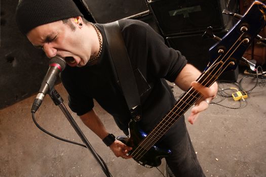 Bassist playing and screaming into a microphone. 
