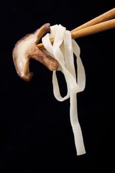 Shitake mushroom and noodles on chop sticks with black background