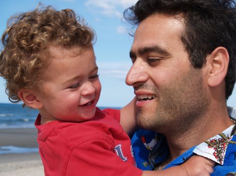 Father holds son close, both smiling enjoying summer beach time.