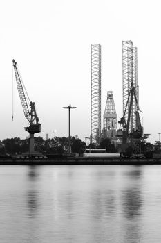 Construction- and ship-repair industry, cranes and drilling rig - vertical black and white image