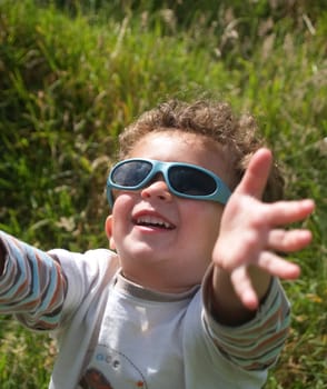 Small boy in sunglasses looking up and hold out his hands, smiling.