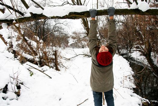 teenage smiling caucasian girl in red cap outdoor over winter snowy tree holding a branch