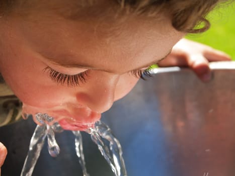 Boy sipping water from a stainless drinking fountain, close up.