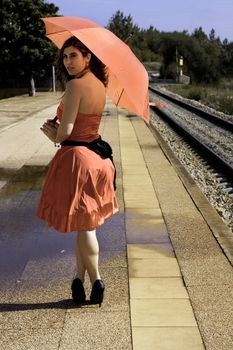 View of a beautiful woman with red dress and umbrella on a train station.