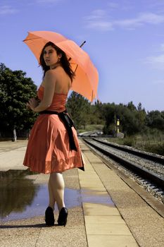 View of a beautiful woman with red dress and umbrella on a train station.