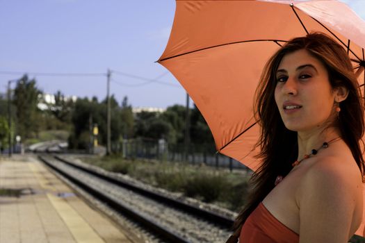 View of a beautiful woman with red dress and umbrella on a train station.