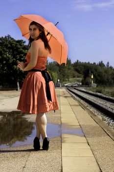 View of a beautiful woman with red dress and umbrella on a train station.